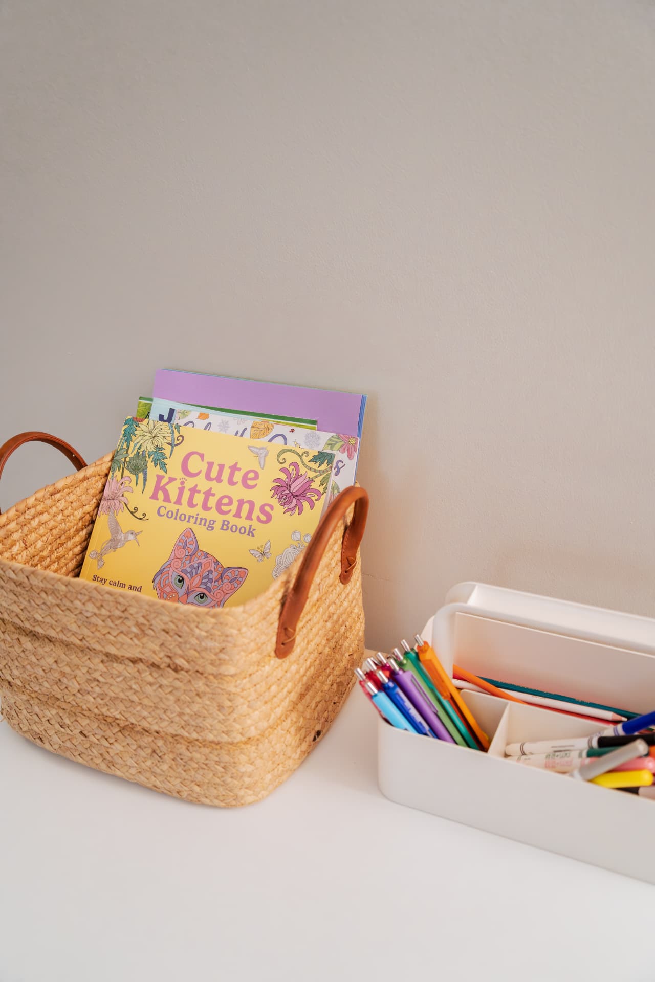 A woven basket of coloring books beside a tray of colored pencils and markers